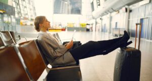 Verspätungen von Airlines und das EU-Recht Frau im Hosenanzug sitzt in Wartehalle mit Beinen auf einem Koffer und wartet auf ihren Flug