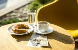 Wie halten Sie es mit Trinkgeld im Urlaub? Ein Tisch mit Kaffee, Kipferl und einigen Münzen und Geldschein als Trinkgeld