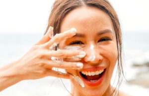 Der richtige Sonnenschutz für jeden Hauttyp Junge Frau cremt ihr Gesicht ein und lacht