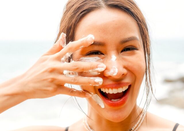 Sonnenschutz für die Haut Junge Frau cremt ihr Gesicht ein und lacht