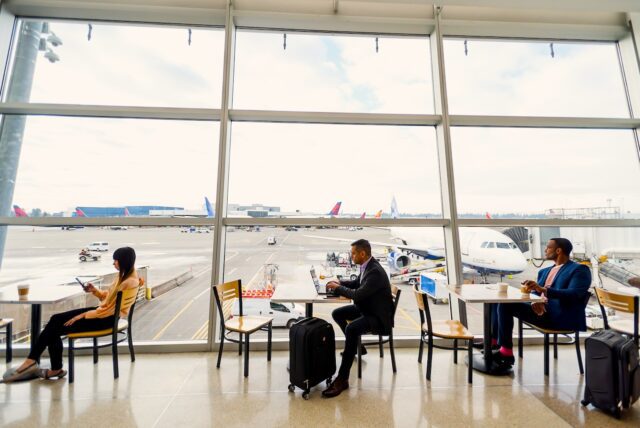 Concur - Airport Gesundheit und Sicherheit für Geschäftsreisende hat Vorrang: Mitarbeiter sitzen in einer Wartehalle am Flughafen mit Blick auf das Vorfeld, wo Jets parken