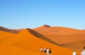 Die Wüste ruft, das Abenteuer der Stille lockt Mehrere Touristen erklimmen eine Düne in der Namib-Wüste