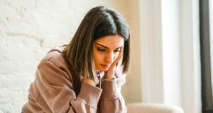 Mehr Urlaubsfrust statt praller Urlaubslust Frustrierte Frau mit langen Haaren stützt ihren Kopf mit beiden Händen auf ihren Knien