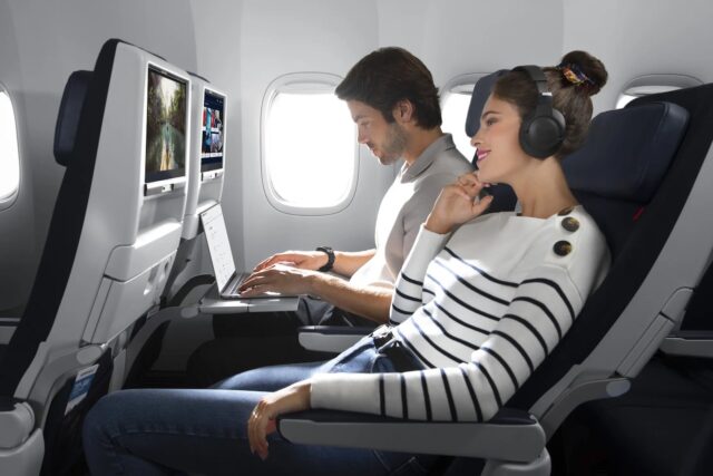 Ultra-High-Speed-WLAN Eine Frau mit Kopfhörer und ein Mann mit Laptop an Bord eines Flugzeuges. Bildschirme auf der Rückseite der Vordersitze