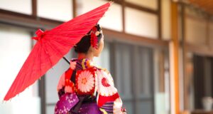 Kultur- und Studienreisen für Wissbegierige Kultur- und Studienreisen nach Asien: Japanisches Mädchen im Kimono und mit rotem Sonnenschirm aus Papier