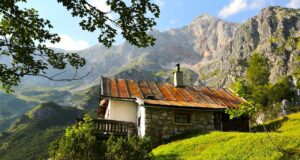 Alpine Destinationen und deren Potenzial Alpine Region mit Bergen und einem Haus auf einem grünen Hügel und einem Strauch vor