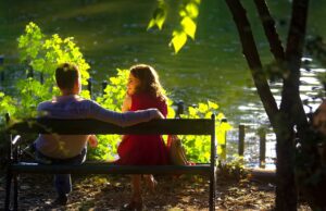 Die Dating-Vorlieben deutscher Urlauber Dating Vorlieben der Deutschen: Ein Paar sitzt auf einer Bank unter einem Baum mit grünen Sträuchern im Vordergrund mit Sonnenlicht