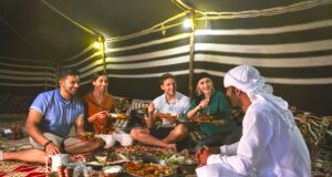 Ramadan in Dubai: Eine kulturelle Reise Vier Touristen sitzen mit einem weiß gekleideten Araber auf dem Boden in einem Zelt und feiern beim Iftar-Essen das Fasteenbrechen