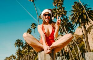 Die Generation Z, die anders reisen will frau-im-roten-tragershirt-und-in-der-schwarzen-sonnenbrille-die-auf-braunem-holzblock-sitzen-