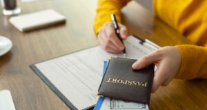 ETA ist für Großbritannien-Reisen notwendig Formulare, Reisepass mit Flugticket und eine Hand mit Kugelschreiber mit einem Formular