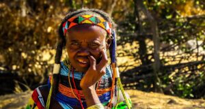 Angola – das verborgene Reisejuwel in Afrika Eine ältere Frau vom Stamm der Mumuila sitzt in ihrer traditionellen Kleidung, mit Frisurund Schmuck