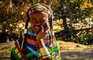 Angola – das verborgene Reisejuwel in Afrika Eine ältere Frau vom Stamm der Mumuila sitzt in ihrer traditionellen Kleidung, mit Frisurund Schmuck