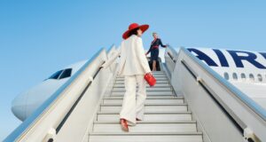 La Première als extravagantes Flugerlebnis Eine Frau in weißem Hosenanzug mit roten Schuhen rotem Hut auf der Gangway:Eleganz und Perfektion erwartet Passagiere in den neuen La Première-Suiten von Air France