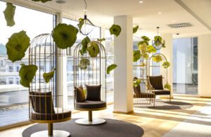 Ein Stadthotel, das aus der Reihe tanzt Vogelkäfigsessel vor großen Fenstern mit Blick auf gegenüberliegende Fassade mit hängenden grünen Blättern