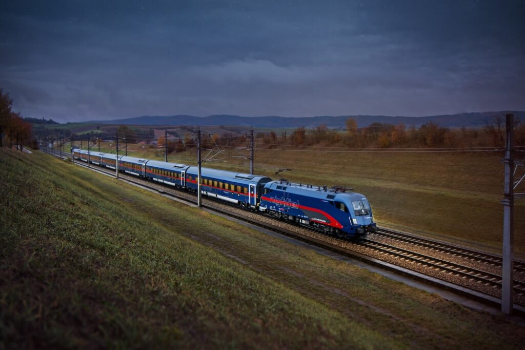 Ein blauer Nachtzug mit einem roten Streifen an der Elektrolok führt durch eine Abendlandschaft
