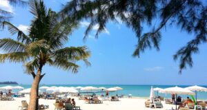 In Phuket den Winter in Europa vergessen! Weißer Sandstrand mit Bäumen, Liegestühlen, Sonnenschirme und türkisfarbenem Meer am Horizont