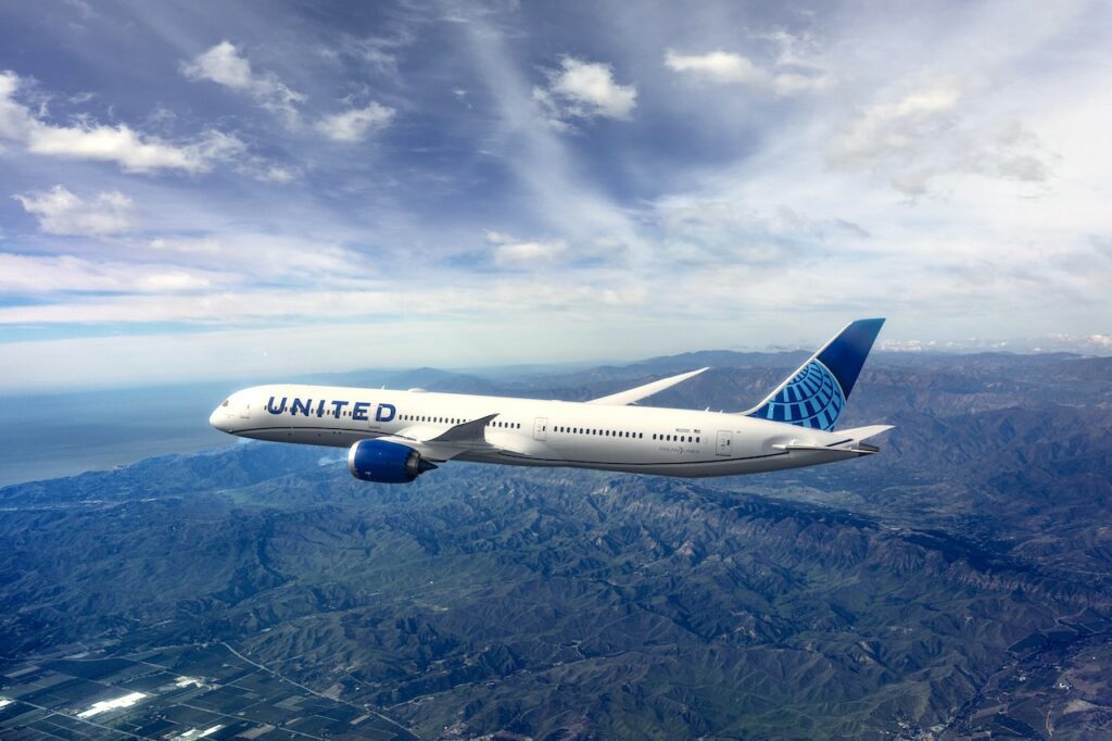 Der neue Dreamliner von United Airlines fliegt über eine bewaldete Landschaft und unterhalb einer grauweißen Wolkendecke