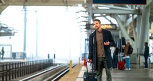 Concur Travel mit SBB auf Geschäftsreisen Concur Travel mit SBB auf Schiene: Mann mit Koffer steht auf einem Bahnsteig und b lockt in Richtung eines einfahren Zuges