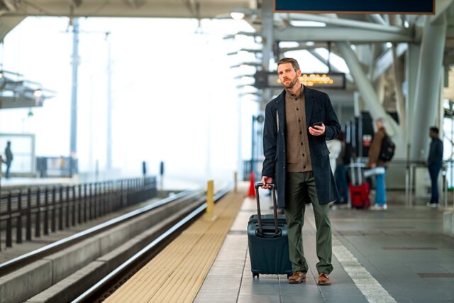 Concur Travel mit SBB auf Schiene: Mann mit Koffer steht auf einem Bahnsteig und b lockt in Richtung eines einfahren Zuges