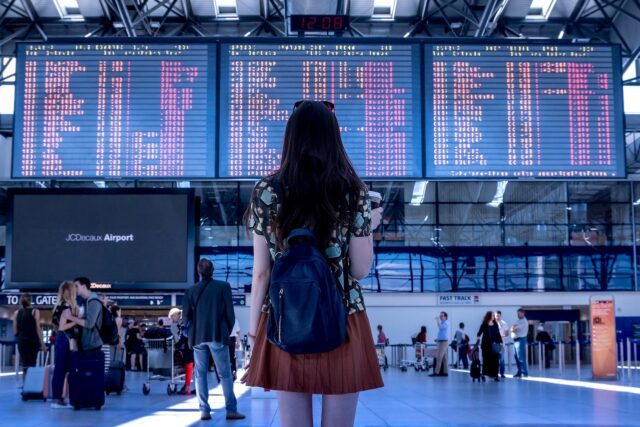 Fluggastrechte sind ein Mindeststandard: Ein Frau mit Rücksack bickt am Flughafen auf eine riesige Anzeigetafel