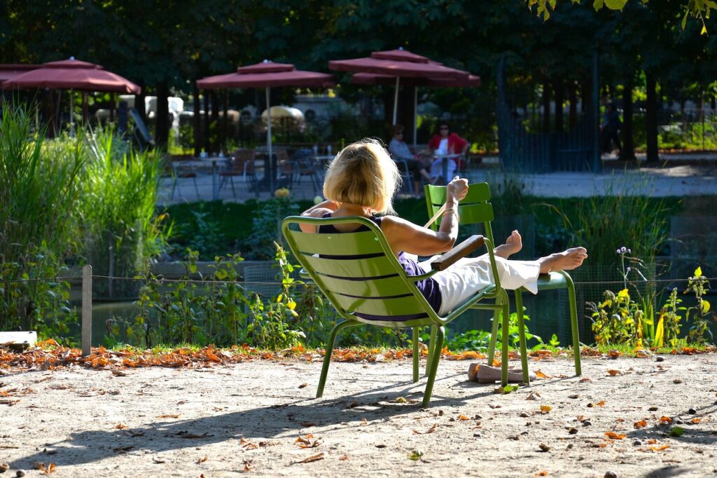 Veranstaltungsplanung mit Pausen: Ein Frau sitzt in der Sonne lässig auf einem grünen Stuhl in einer Hotelanlage und ruht sich von einem Seminar aus