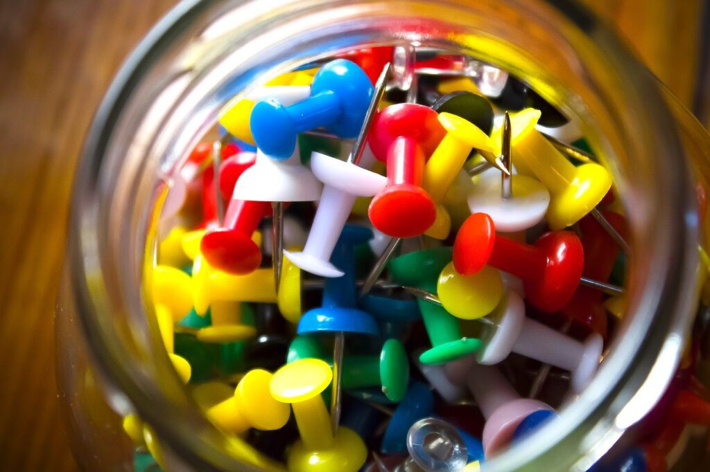 Wichtig bei der Veranstaltungsplanung: Eine Schale mit vielen bunten, blauen, roten, gelben, grünen und blauen Pinnadeln