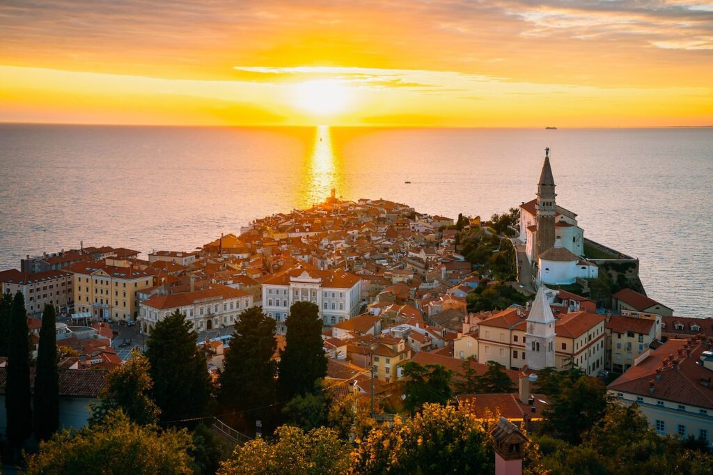 Die slowenischen Hafenstadt Piran mit dem den Ort überragenden Kirchturm im Licht der untergehenden Sonne