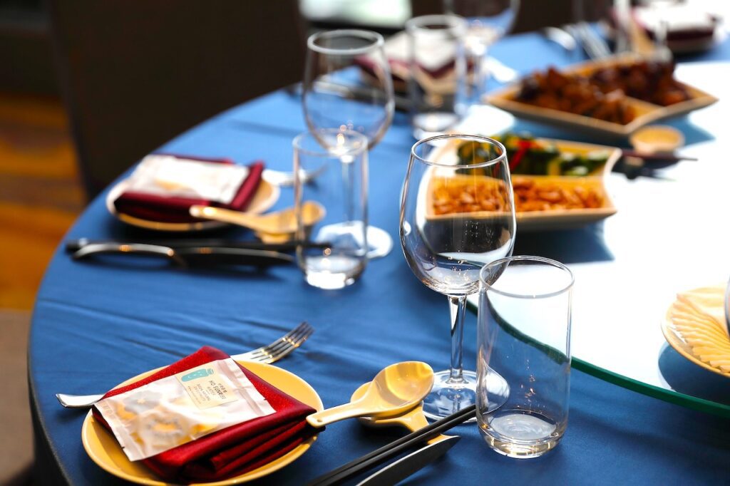Das richtige Table Setting bei der Veranstaltungsplanung führt zum Erfolg: Ein gedeckter Tisch, blaues Tischtuch, Teller mit roten Servietten und Gläsern und Besteck