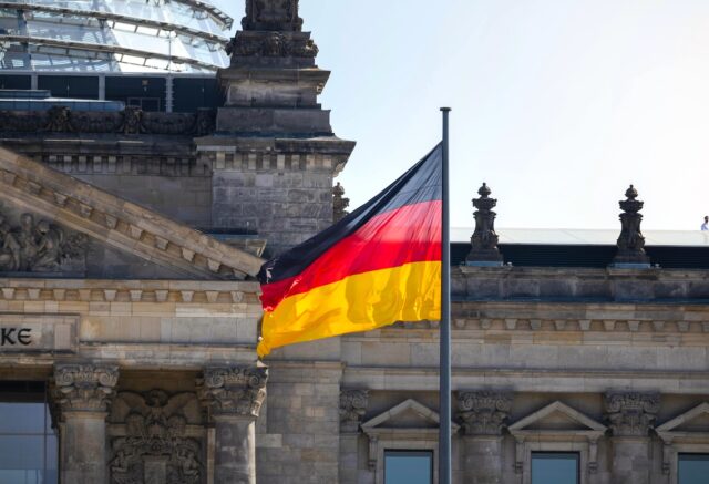 Warum reisen Österreicher nach Deutschland? Österreicher fasziniert von Deutschland: Bundestagsgebäude mit Glaskuppe und Deutschlandfahne davor