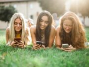 Social Media im Urlaub? Ja, warum nicht! Social Media im Urlaub: Drei junge Frauen liegen auf dem Rasen und durchsuchen ihre Smartphones nach Neuigkeiten aus Social Media