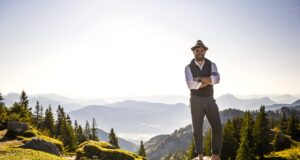 Bayern – direkt, kompetent und persönlich! Ein Mann mit Hut steht auf einem Berg in Bayern mit verschränkten Armen