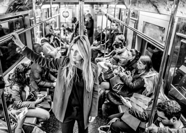 Läm in der U-Bahn in New York. Menschen sitzen eng beieinander und Telefon ihren mit Smartphones, eine Blondine steht im Vordergrund