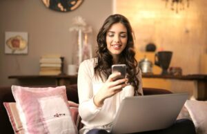 Last Minute-Urlaub, aber richtig buchen! Last Minute-Bhcung: Junge Frau sitzt auf einem Sofa mit Handy und Laptop auf dem Schoss
