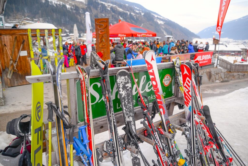Bergstation mit vielen Gästen, die ihre Ski an ein Plakat abgestellt haben