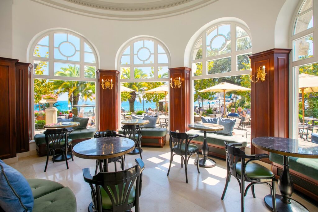 Kuppelsaal mit Kaffeehaustischen und bBlick auf Palmen und Meer