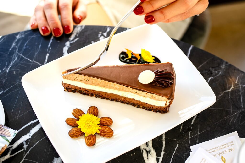 Ein Tortenstück mit <creme, eine <hand mit roten Fingernägel und einer Gabel 