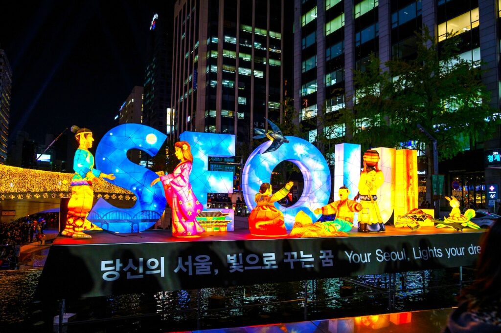 Beleuchtete Buchstaben, die das Wort Seoul bilden, mit Figuren in koreanischer Nationaltracht in der Hauptstadt von Korea