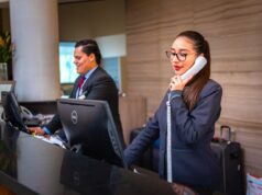 Sind Businessreisende zufrieden mit Hotels? Businessreisen zufrieden mit Hotels? Zwei Rezeptionisten, eine Frau telefoniert, ein Mann blickt auf einen Bildschirm