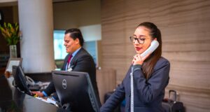 Sind Businessreisende zufrieden mit Hotels? Businessreisen zufrieden mit Hotels? Zwei Rezeptionisten, eine Frau telefoniert, ein Mann blickt auf einen Bildschirm