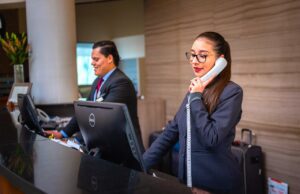 Sind Businessreisende zufrieden mit Hotels? Businessreisen zufrieden mit Hotels? Zwei Rezeptionisten, eine Frau telefoniert, ein Mann blickt auf einen Bildschirm