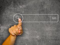 Wie digitale Quellen Urlauber beeinflussen Digitale Quellen als Helfer: Vor einer dunklen Schiefertafel zeigt der Daumen einer Hand auf ein Suchfeld