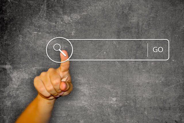 Digitale Quellen als Helfer: Vor einer dunklen Schiefertafel zeigt der Daumen einer Hand auf ein Suchfeld