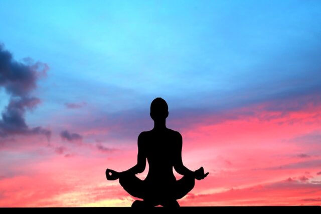 Garmisch-Partenkrichen im Yoga-Flow Sonnenuntergang und eine Frau hock in einer Yoga-Pose und blickt auf dem blauen Himmel mit dem rötlichen Licht der untergehenden Sonne