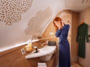 Travel Awards für Emirates als Best Airline Travel Awards für Emirates: Eine Frau im bleuen Kleid steht in einer Toilette an Bord von Emirates und kämmt ihr Haar