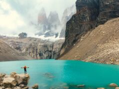 Chile: Ziel für Abenteurer und Naturfreunde Zwischen Bergen, Gletschern und endlosem Himmel erstrecken sich in Chile die Torres del Paine, die „Türme des blauen Himmels“, im Nationalpark : Eine Person steht auf einem Felsvorsprung und blickt auf den grünen See mit dem nebelverhangenen Schneegipferln