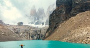 Chile: Ziel für Abenteurer und Naturfreunde Zwischen Bergen, Gletschern und endlosem Himmel erstrecken sich in Chile die Torres del Paine, die „Türme des blauen Himmels“, im Nationalpark : Eine Person steht auf einem Felsvorsprung und blickt auf den grünen See mit dem nebelverhangenen Schneegipferln
