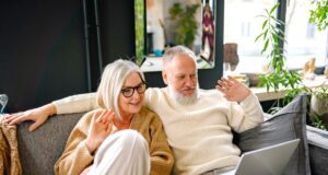 Best Ager als lukrative Zielgruppe im Focus Ein älteres Paar – Best Ager – sitzt lässig auf einem Sofa und blickt auf das Display eines Laptops