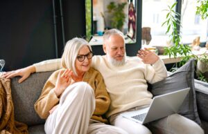 Best Ager als lukrative Zielgruppe im Focus Ein älteres Paar – Best Ager – sitzt lässig auf einem Sofa und blickt auf das Display eines Laptops