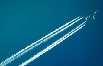 Dekarbonisierung der Luftfahrt unbezahlbar Dekarbonisierung: Passagiere am blauen Himmel mit Kondensstreifen