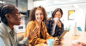 So ticken Gen Z und Boomer auf Geschäftsreisen Gen Z und Boomer: Junge Frauen und ein dunkelhäutiger Mann sitzen an einem Tisch und unterhalten sich